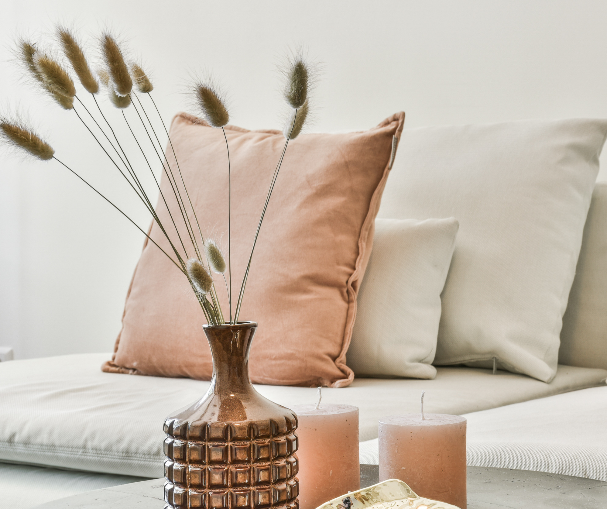 sofa avec coussins roses, chandelles roses et vase avec branche de blé