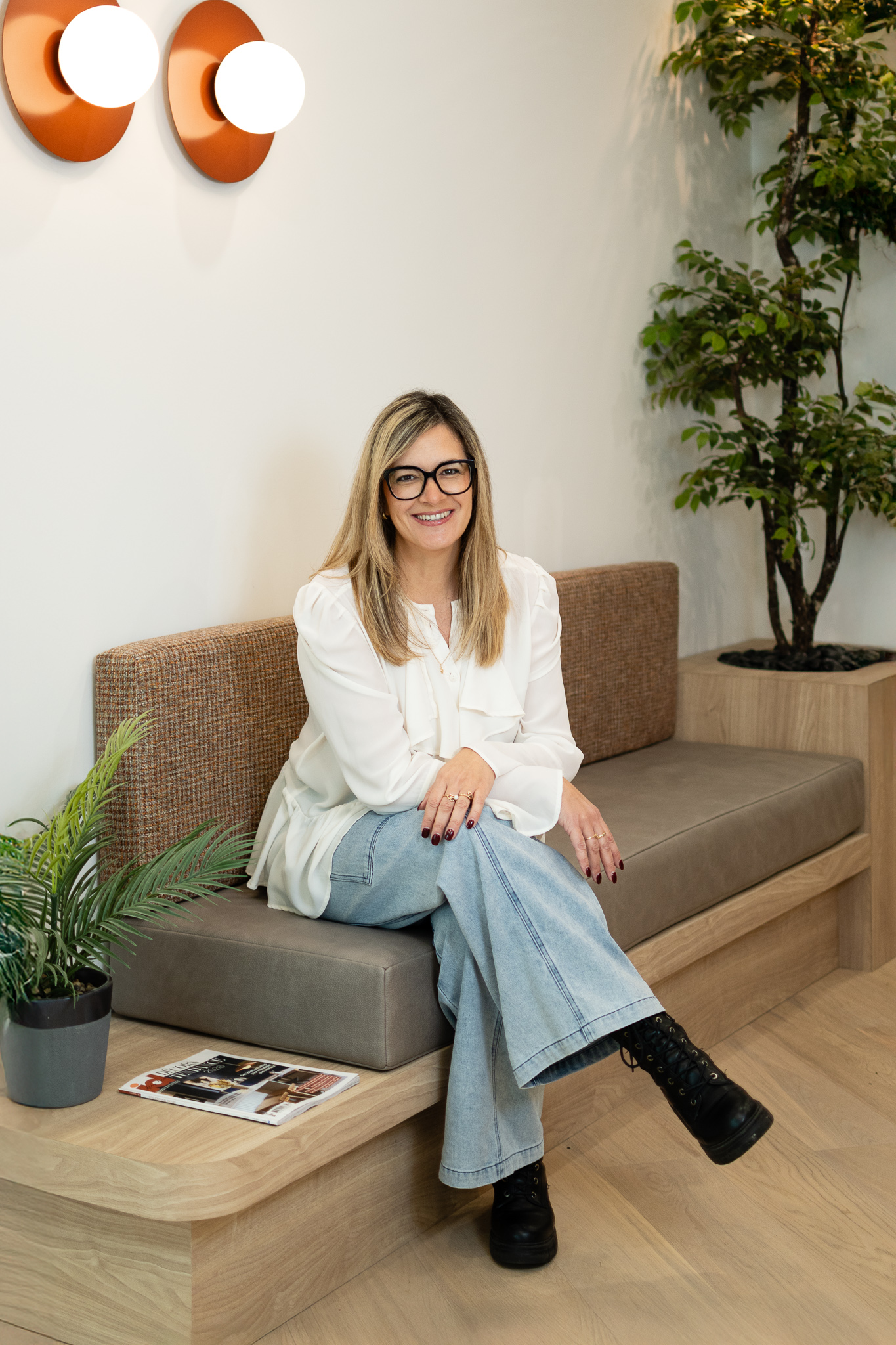 Femme souriante, jambe croisée, sur sofa beige avec plantes et revue déco