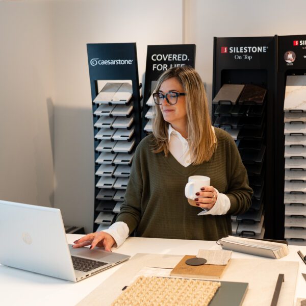 femme souriante devant comptoir de matériaux et de couleurs, designer, tasse de café à la main