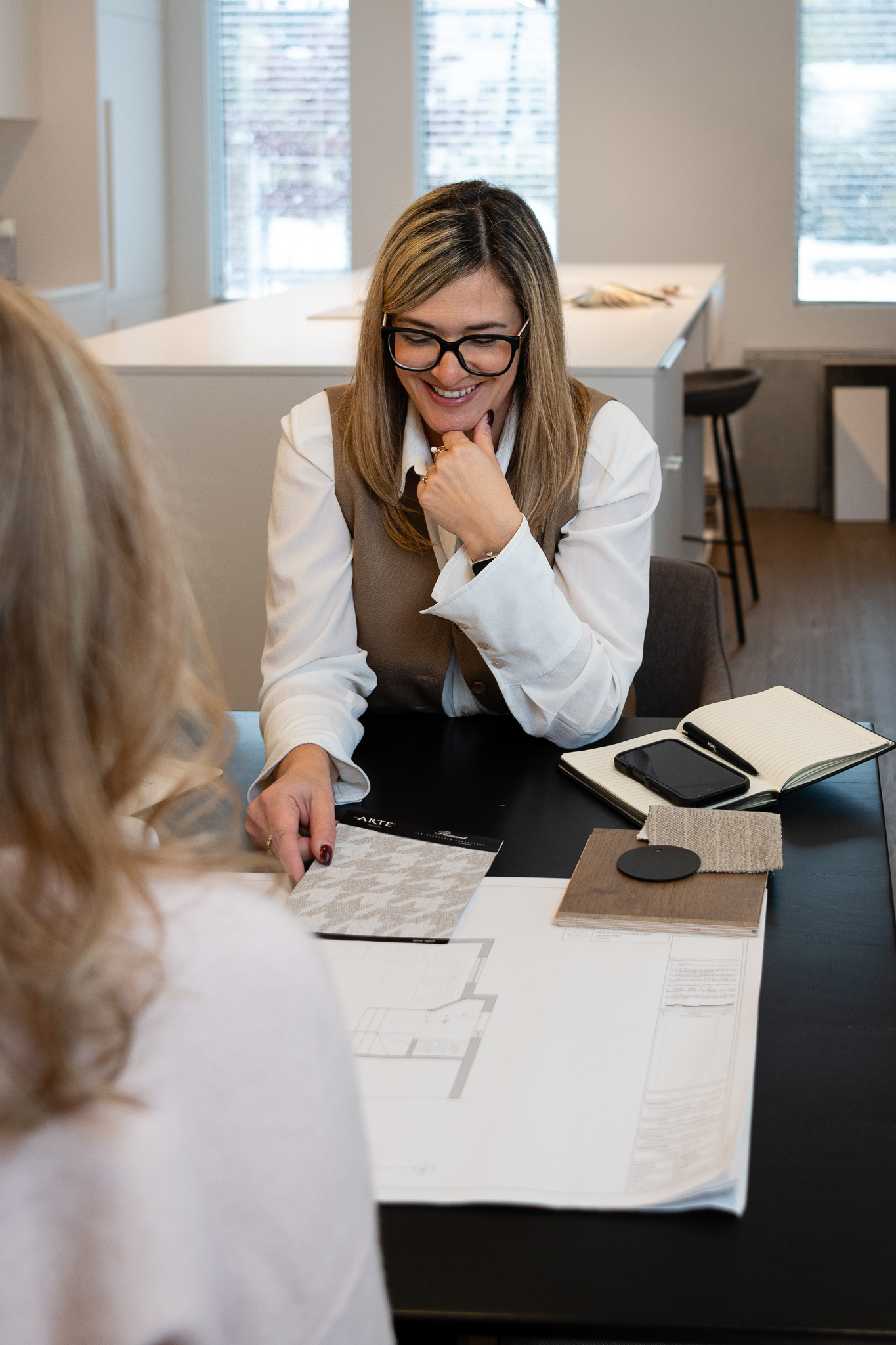 femme souriante devant comptoir de matériaux et de couleurs, designer en rencontre avec une cliente
