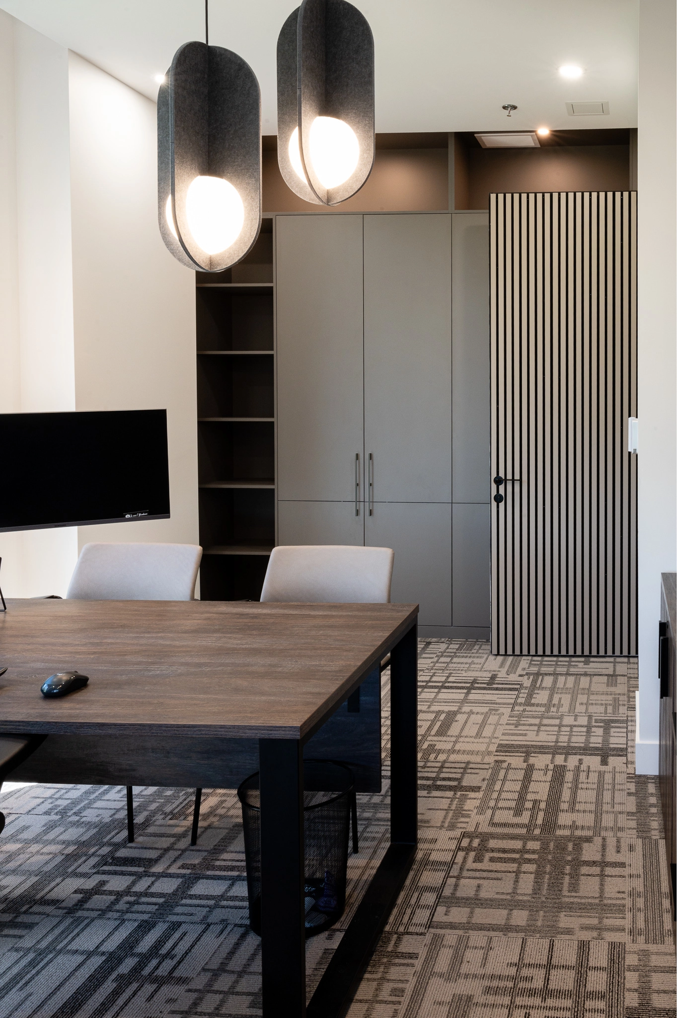 Bureau professionnel chaleureux avec grand rangement vertical, luminaire suspendu, grande fenestration et bureaud e travail en bois.