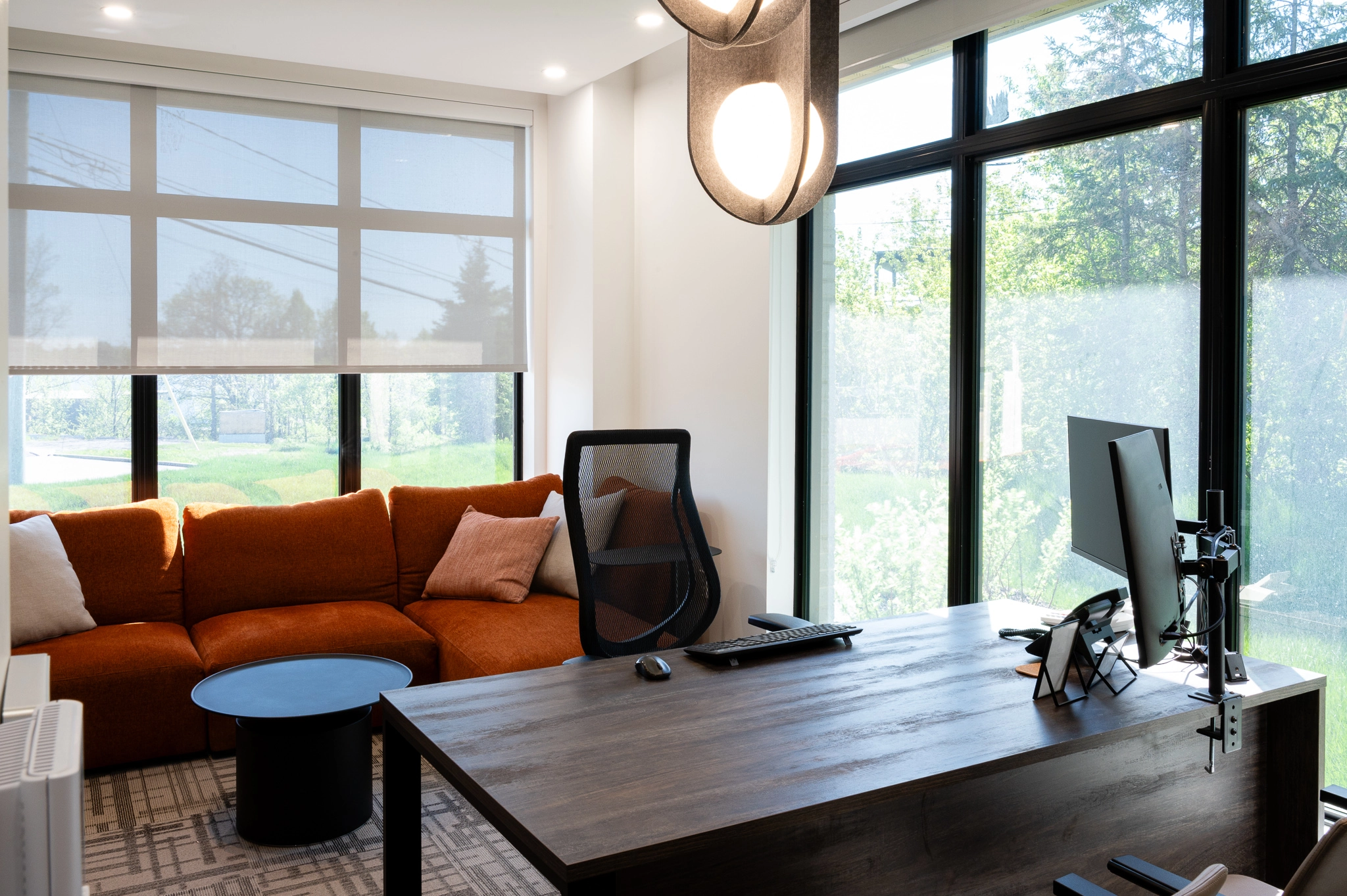 Bureau professionnel chaleureux avec fauteuil cuivré, luminaire suspendu, grande fenestration et bureaud e travail en bois