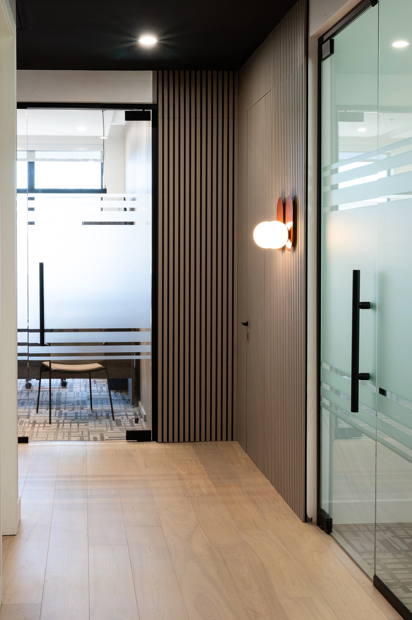 Corridor d'un espace de bureaux commerciaux, lattes de bois murales, luminaires orangés, portes vitrées